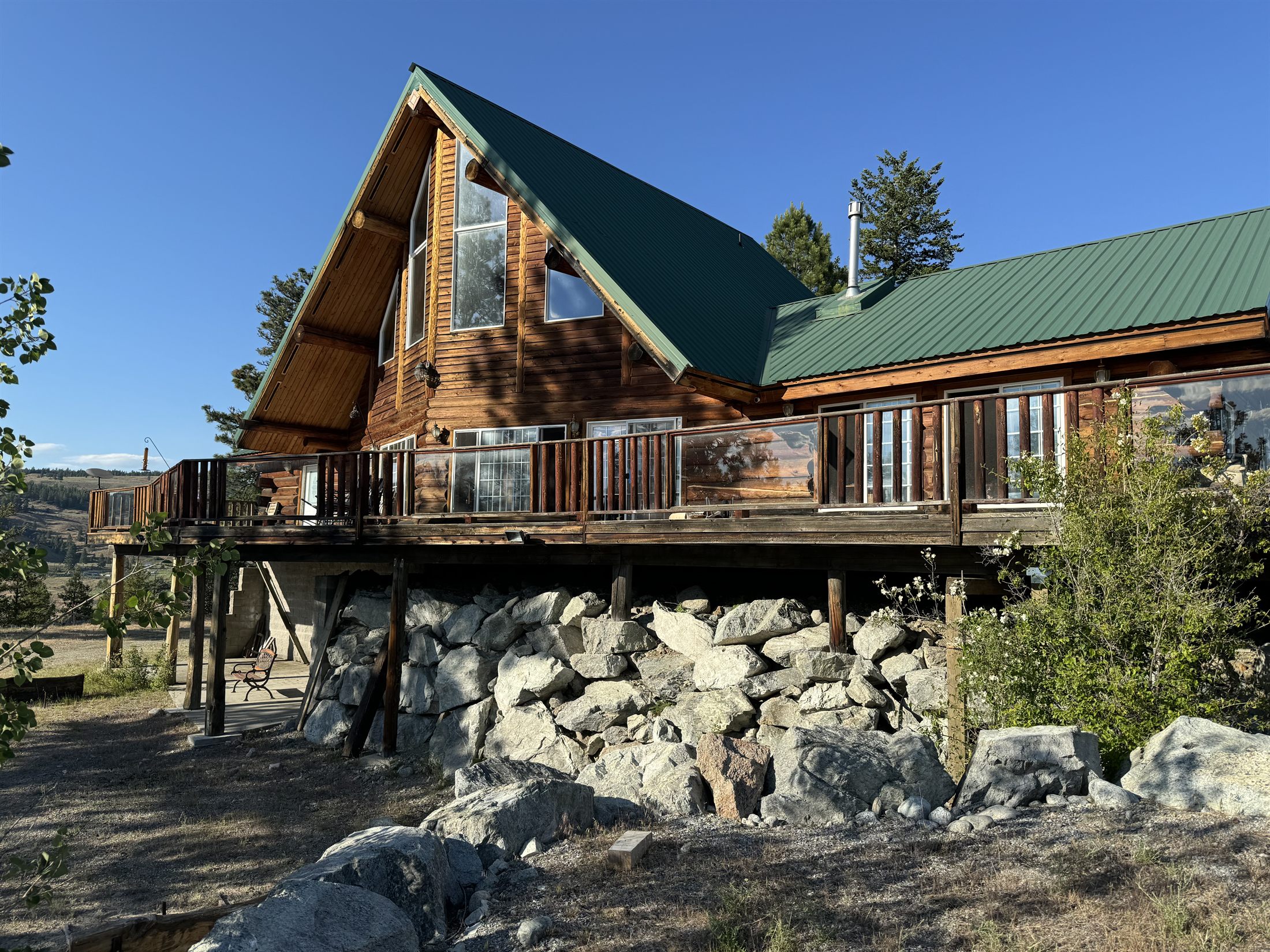 The log home at 20 Homestead Spur on its rock foundation, with a wraparound deck and mountain views under a summer sky.