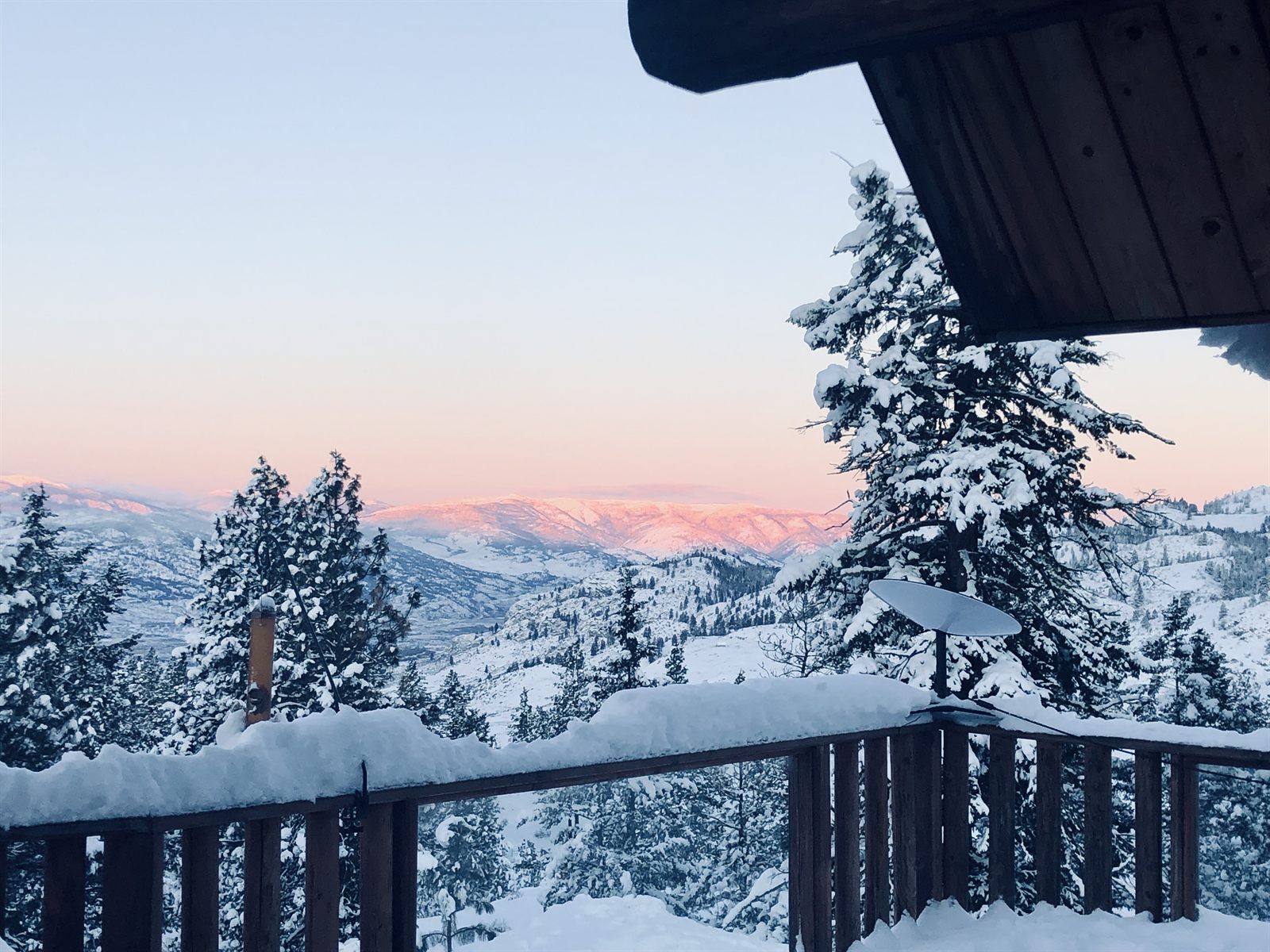 Snow on the deck rail with pink alpenglow on the mountains.