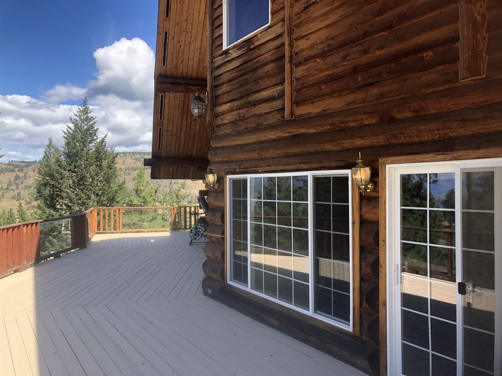 The wraparound deck and log wall with pines and mountains beyond.