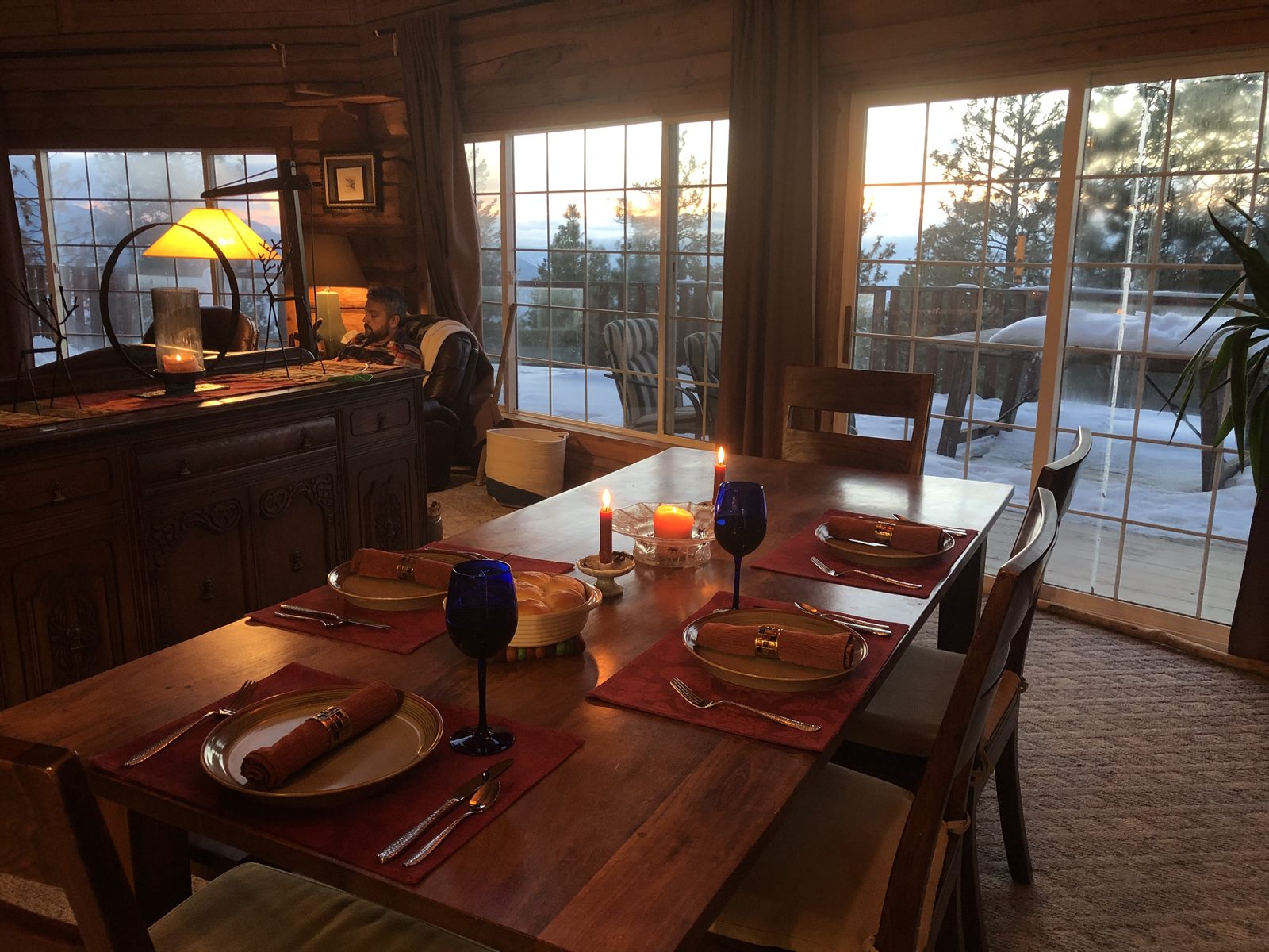 A candlelit dining table by the windows with a snowy view beyond.