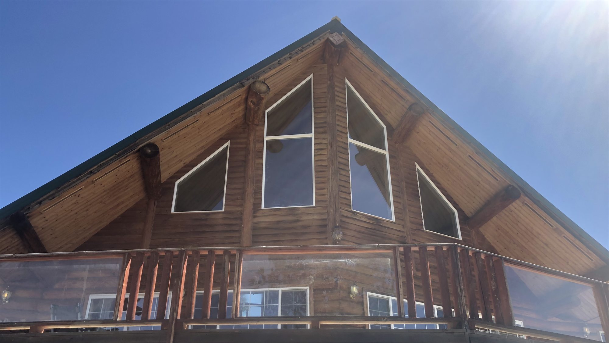 The log home's A-frame gable and wraparound deck against a clear sky.
